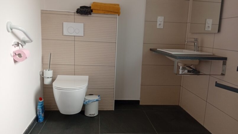 salle de bain PMR accessible aux fauteuils roulants, WC avec barre d'appui et espace de transfert et lavabo sans meuble dessous